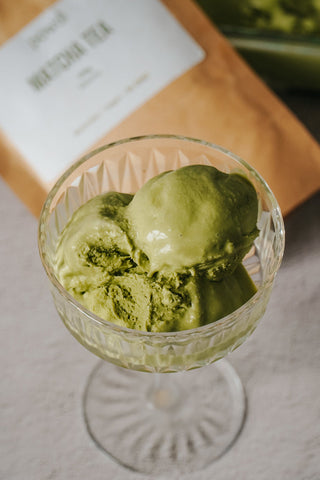 Matcha green tea ice cream scoops in a glass cup with matcha tea powder packet in background
