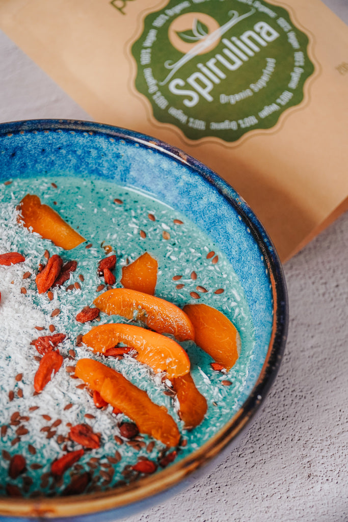 Mėlynosios spirulinos kokteilio dubenėlis su persikais ir kokoso drožlėmis