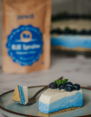 Blue spirulina cheesecake slice topped with blueberries on a plate, package in background