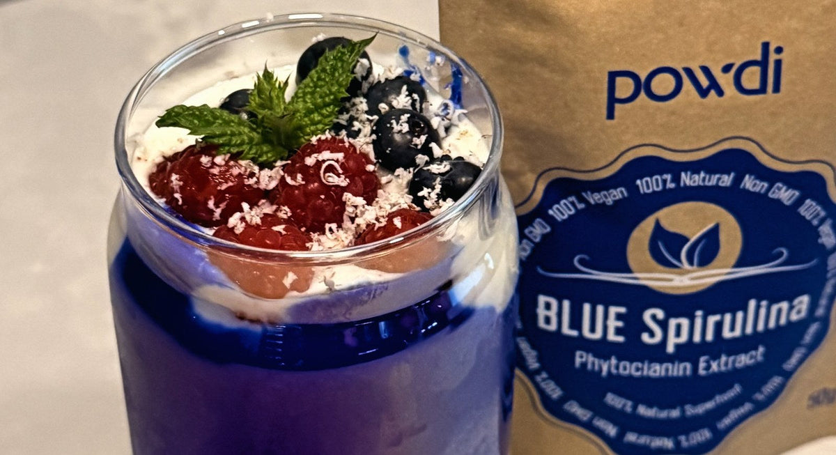 Naminis graikiškas jogurtas su mėlynąja spirulina ir uogomis šalia Powdi Blue Spirulina pakuotės