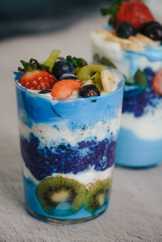 Colorful spirulina breakfast parfait with chia pudding, yogurt, fresh kiwi, strawberries, and blueberries in a glass.